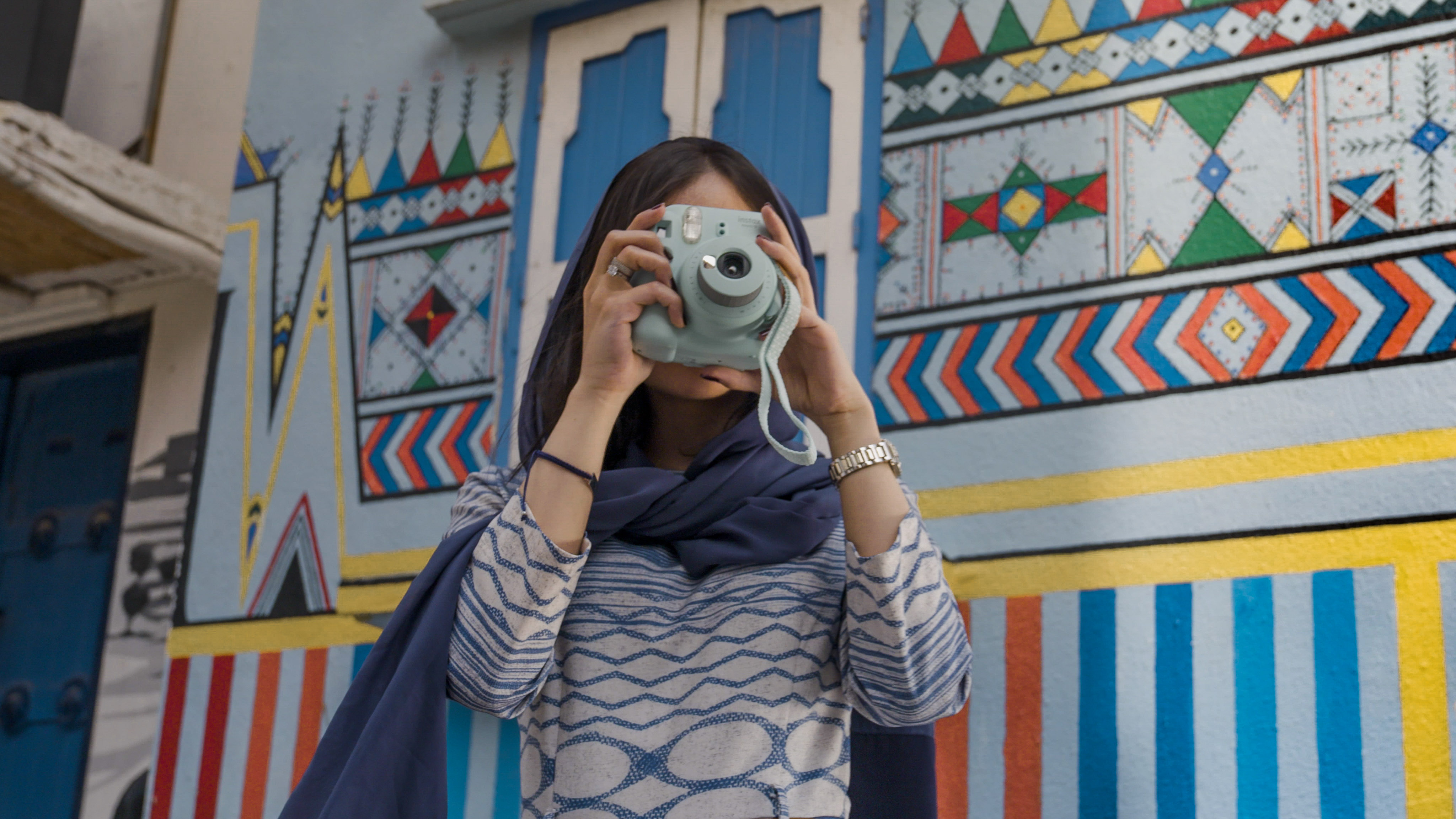 Woman taking a photo in front of colourful Al-Qatt Al-Asiri mural art in Abha, Saudi Arabia