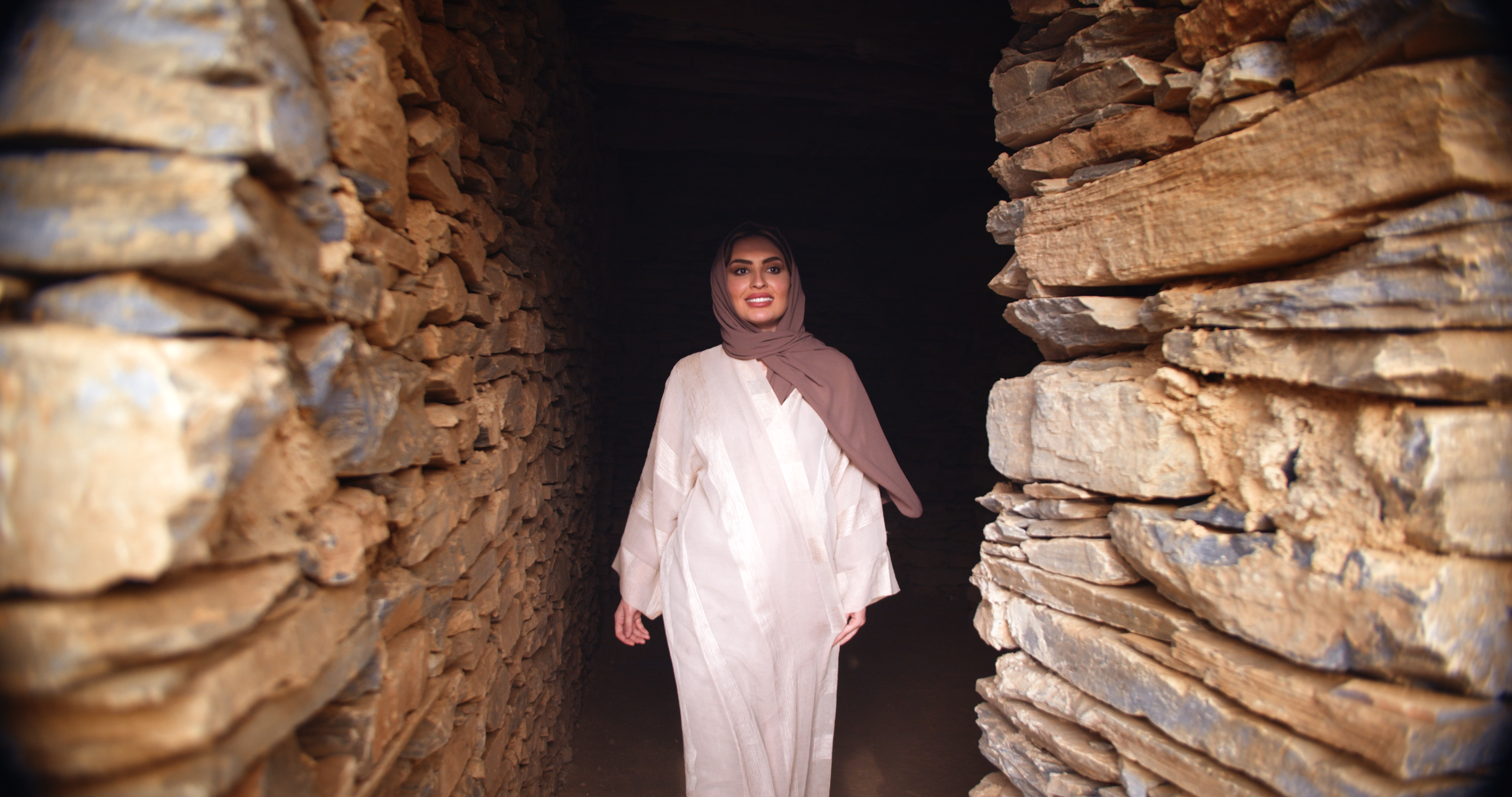 Saudi woman in hijab walking through a traditional stone passage in Rijal Almaa heritage village