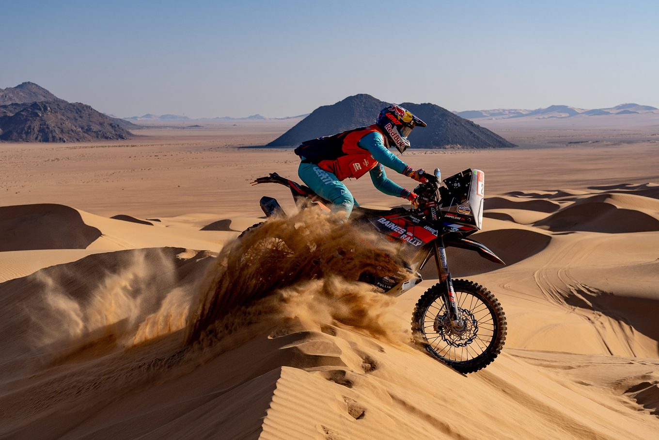 Rally motorbike jumping over a dune crest at the Dakar in Saudi Arabia